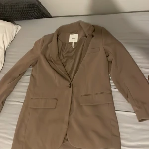 Beige kavaj från Object - Stilren beige kavaj från Object med klassisk krage och en knapp framtill. Kavajen har två fickor med lock och en bröstficka. Perfekt för en snygg och uppklädd look.