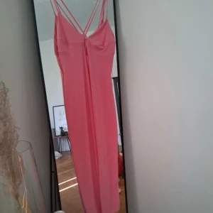 Lång rosa klänning med smala axelband - Säljer en lång, stilren rosa klänning med smala dubbla axelband och v-ringad front. Klänningen har en elegant, rak passform och är perfekt för dig som gillar minimalistisk och trendig stil. 