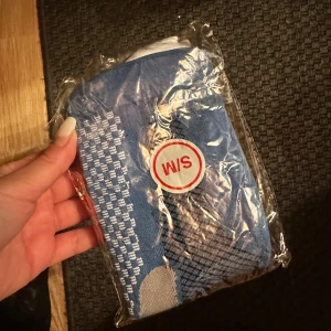 Blå och grå sportstrumpor W/S stödstrumpor  - Blå och grå/vit strumpor i storlek L/XL, perfekta för träning. Strumporna har ett rutigt mönster upptill och är tillverkade i mjukt och slitstarkt material, troligen bomull och polyester. Snygg design med kontrastfärg vid häl och tå.Dessa strumpor erbjuder överlägsen komfort och stöd. Tillverkade av högkvalitativt, fukttransporterande tyg håller de dina fötter torra och svala. Kompressionstekniken ger optimalt stöd för att förbättra blodcirkulationen, minska muskeltrötthet och förebygga skador.