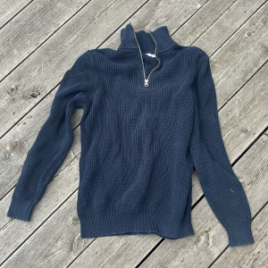 Mörkblå stickad tröja med half zip - Snygg mörkblå stickad tröja med ribbad struktur och hög krage. Tröjan har en praktisk half zip-dragkedja framtill och långa ärmar. Perfekt för lager-på-lager under kyliga dagar.