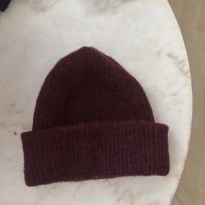 Vinröd stickad mössa från Åhléns - Mysig vinröd mössa från Åhléns med klassisk uppvikt kant. Stickad i ett mjukt och värmande material som passar perfekt när det är kallt ute. Enkel och stilren design som funkar till det mesta.