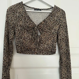 Leopardmönstrad croppad topp  - Säljer en croppad långärmad topp från Shein med leopardmönster i beige, brunt och svart. Toppen har v-ringning och snygg knytning framtill. Perfekt för dig som vill sticka ut med ett djurmönstrat plagg.