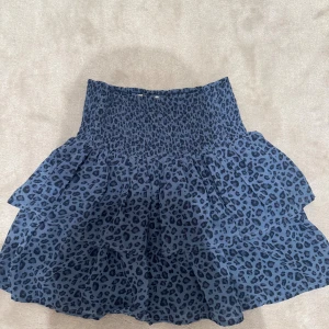 Blå volangkjol med leopardmönster - Supersöt blå kortkjol med svart leopardmönster och volanger. 