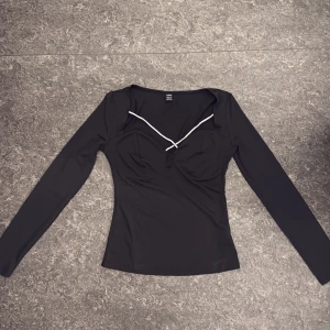 Svart långärmad topp med strassdetalj - Svart långärmad topp från SHEIN i storlek S. Toppen har en figurnära passform, byst med markerade kupor och en snygg strassdetalj som går i ett kryss över urringningen. Perfekt för dig som vill sticka ut lite extra.