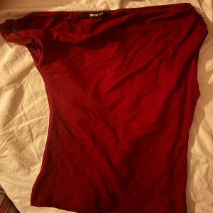 Röd asymmetrisk topp från Gina Tricot - Säljer en röd asymmetrisk topp från Gina Tricot i storlek S. Toppen har en cool one shoulder-design och är tillverkad i mjuk bomullsmix. Perfekt för dig som vill sticka ut med en enkel men trendig look.