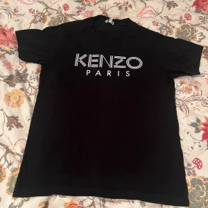 Svart Kenzo Paris t-shirt - Svart t-shirt från Kenzo med stort vitt logotryck 'KENZO PARIS' på bröstet. Strl XS. Tröjan är i bra skick.