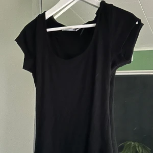 Svart ribbad topp  - En svart ribbad topp från Kappahl i storlek M. Toppen har rundad halsringning och korta ärmar. Den är figurnära och tillverkad i ett mjukt, stretchigt material som passar perfekt till jeans eller kjol.