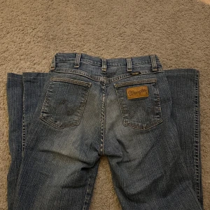 Wrangler blå jeans med dragkedjedetalj - Snygga blå jeans från Wrangler i klassisk tvätt med dragkedjedetalj vid fickan. Bootcut, fem fickor. Tillverkade i bomull. Nyskick