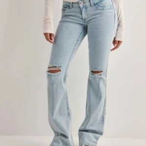 Low waist Bootcut ljusblå jeans - Snygga ljusblå bootcut jeans från Nelly i storlek 34. Jeansen är använda fåtal gånger och är i bra skick. Dom har slitningar på knäna och rosa detaljer på fickorna. Jeansen är stretchiga och har en låg midja 💗