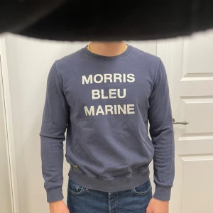 Blå sweatshirt från Morris, strl M - Säljer en marinblå sweatshirt från Morris med trycket 'MORRIS BLEU MARINE' på bröstet. Tröjan har rund hals, långa ärmar och ribbade muddar. Perfekt för dig som gillar stilren och enkel design med en touch av preppy vibe.
