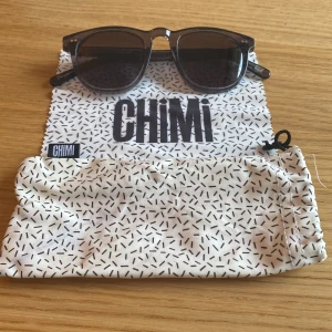 Svarta solglasögon från Chimi - Snygga svarta solglasögon från Chimi med klassisk rundad form och mörka glas. Bågarna är i plast och kommer med originalfodral och putsduk med svartvitt mönster. Perfekta för att lyfta din stil i sommar.