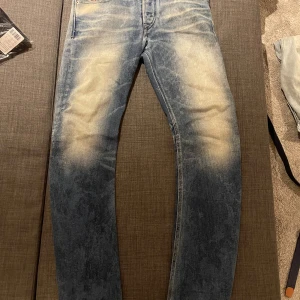 Diesel  blå jeans - Säljer ett par Diesel  jeans i blå tvätt med tydlig blekning och slitningar på framsida och bakfickor. Klassisk femficksmodell med raka ben och stretchigt denimtyg för extra komfort. Snyggt läderpatch bak i midjan. Ritkigt feta, blekningen sitter riktigt bra när man har på sig de W28 L34
