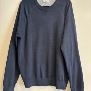 Marinblå stickad tröja från Mango - En stilren marinblå stickad tröja från Mango med rund halsringning och ribbade muddar vid ärmslut och nederkant. Tröjan har en klassisk passform och är perfekt för lager-på-lager under kyligare dagar. Tröjan är endast använd 1 gång. Nyskick. 