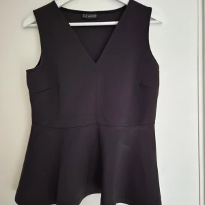 Svart peplumtop från Bodyflirt - Svart, ärmlös peplumtop från Bodyflirt med v-ringning. Toppen har markerad midja och utsvängd nederdel. 