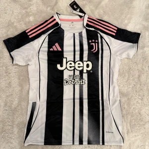 Juventus randig fotbollströja Adidas - Juventus fotbollströja från Adidas med svartvita ränder och rosa detaljer på axlarna. Jeep-logga på bröstet och tre rosa stjärnor vid klubbmärket. Tillverkad i lätt polyester med Aeroready-teknologi för bra ventilation. Snygg passform och korta ärmar.