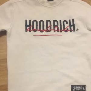 Vit Hoodrich sweatshirt XS - Säljer en vit sweatshirt från Hoodrich i storlek XS. Tröjan har tryckt logga i svart och rött framtill samt patch nertill. Mjuk insida och långa ärmar, perfekt för en clean streetwear-look. Finns lite färg på tröjan, finns bild. Men går bort med lite klor.