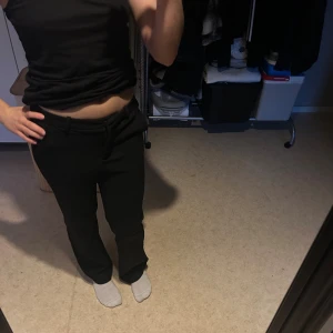 Svarta kostymbyxor med raka ben - Säljer ett par svarta kostymbyxor med raka ben och bälteshällor. Byxorna har en klassisk passform, perfekta för en clean och stilren look. Materialet känns mjukt och följsamt, och de stängs med dragkedja och hake framtill. Storlek passar mella xs till s