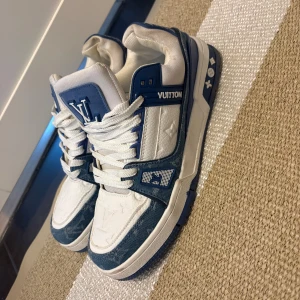 Louis Vuitton blåvita sneakers - Säljer ett par riktigt snygga Louis Vuitton sneakers i blått och vitt med tydliga LV-loggor. Skorna har klassisk snörning, rund tå och platt sula. Materialmix av skinn och textil med monogramdetaljer och coola kontraster. Perfekta för dig som vill sticka ut med lyxig streetstyle.