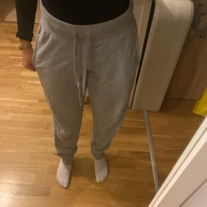 Grå mjukisbyxor med snörning - Säljer ett par grå mjukisbyxor med bred resår i midjan och snörning framtill. Byxorna har en loose passform med muddar vid bensluten och är noppriga (inte tydligt) Strl M men passar bra till mig som är XS
