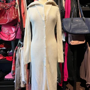 Vit lång stickad kofta från Vero Moda - Snygg lång stickad kofta från Vero Moda. Plagget har långa ärmar, stor krage och knappar hela vägen framtill. Den är figurnära och har en ribbad detalj vid halsen. 