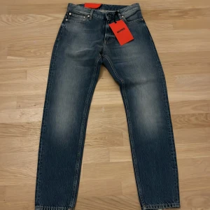 Blå croppade jeans från Whyred - Snygga blå jeans från Whyred med croppad benlängd och hög midja. Modellen har tapered fit och klassisk femficksdesign. Jeansen är tillverkade i denim och har en cool tvättad look med ljusare partier framtill.