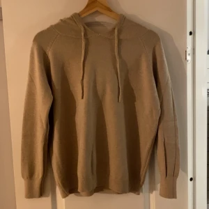 Beige stickad hoodie av merinoull - Säljer en beige stickad hoodie av merinoull med huva och snörning som jag aldrig använt då den var för liten för mig. Tröjan har långa ärmar och ribbade muddar vid ärmslut och nederkant. Perfekt för dig som gillar en enkel och stilren look med en mysig känsla. Storlek S men kan passa XS också, hör av er vid frågor och funderingar!