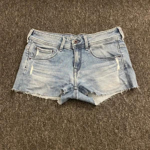 Blå jeansshorts från Pepe Jeans - Snygga blå jeansshorts från Pepe Jeans med rå kant och slitningar framtill. Klassisk femficksmodell med knapp och dragkedja. Bakfickorna har coolt broderat vågmönster. Shortsen är gjorda i bomull med lite stretch för skön passform.