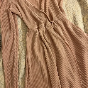 Plisserad ljusrosa omlottklänning NLY - Superfin plisserad ljusrosa omlottklänning från NLY Trend. Klänningen har långa ärmar, markerad midja och ett glansigt tyg som ger en lyxig känsla. 