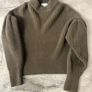 Olivgrön stickad tröja från H&M - Säljer en olivgrön stickad tröja från H&M med bred ribbstickning och puffiga långärmar. Tröjan har hög hals och en loose fit som ger en cool och avslappnad vibe. 