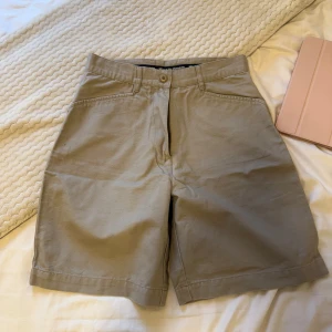 Beige bomullsshorts från Best in Town - Klassiska beige shorts från Best in Town i 100% bomull. Modellen har normal passform, raka ben och praktiska fickor både fram och bak med knappdetaljer.
