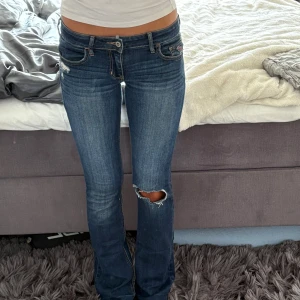 Unika lågmidjade bootcut jeans 💕 - Snygga mörkblå jeans med bootcut passform och låg midja. Jeansen har slitningar och hål på ena knät samt lätt slitna detaljer vid fickorna. Jeansen är från holismen köpta i USA för 2 månader sedan använda 3 gånger, skriv gärna för frågor💕