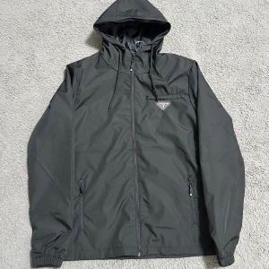 Pr@da Jacka  - En fin svart windbreaker med ett unikt märke på bröstet. Fint material!