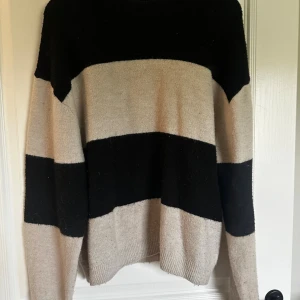 Randig stickad tröja från H&M - Säljer en stickad tröja från H&M med breda svarta och beige ränder. Tröjan har lång ärm, rund halsringning och är supermjuk och chill att bära. Perfekt för lager-på-lager och passar till jeans eller leggings.