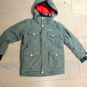 Grön parkajacka från North Bend - Snygg grön parkajacka från North Bend med huva och röd insida. Jackan har fyra stora fickor med knappar, dragkedja och tryckknappar framtill. Perfekt för kalla dagar och har en cool, urban look som passar dig som gillar funktion och stil.