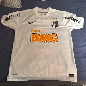 Santos FC Neymar Jr 11 Nike Dri-Fit tröja - Vit kortärmad fotbollströja från Santos FC med Neymar Jr och nummer 11 på ryggen. Nike Dri-Fit material för skön känsla och ventilation. Snygga tryck med klubbmärke, sponsorer och detaljer i svart och orange. Perfekt för dig som älskar brasiliansk fotboll och Neymar.