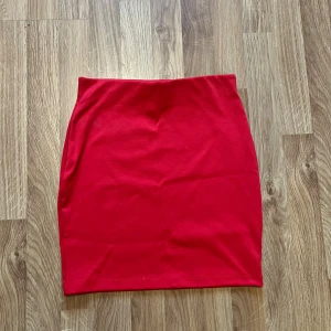 Röd kortkjol från Cubus  -  röd kortkjol från Cubus. Kjolen har en enkel, tight passform och är helt utan mönster eller detaljer. Oanvänd