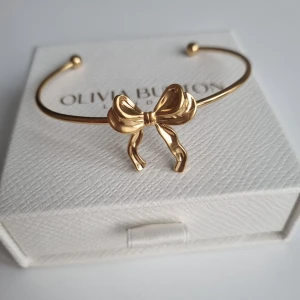 Guldfärgat armband med rosett - Superfint armband från i guldfärg med en söt rosett framtill. Stilren och feminin design som verkligen sticker ut på handleden. Perfekt accessoar för dig som gillar detaljer med lite extra charm. Lådan ingår ej.