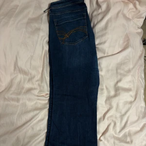 bootcut jeans blå low rise  - Säljer ett par klassiska jeans i mörkblå tvätt med bootcut passform. Snygga kontrastsömmar i orange. Jeansen har fem fickor och är tillverkade i robust denim.