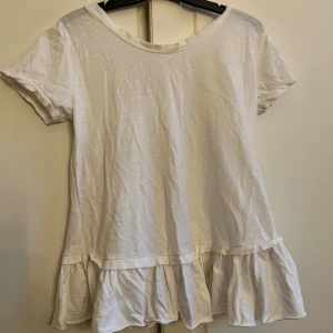 Vit T-shirt med volang och V ringing - Vit, V-ringad T-shirt. Det står tyvärr ingen lapp vart den är ifrån eller storlek