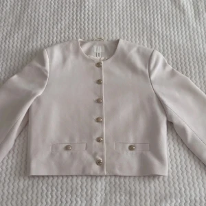 Vit jacka/kavaj med guldknappar  - Stilren vit kavaj från H&M med rund halsringning och dekorativa guldknappar framtill 