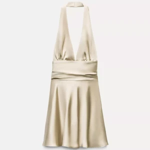 Champagnefärgad halterneck klänning - Snygg kort klänning i champagnefärgad satin med halterneck och djup v-ringning. Klänningen har en bred midjedetalj och ett glansigt, lyxigt material som ger en elegant look. Perfekt för dig som vill sticka ut med en stilren och trendig outfit.