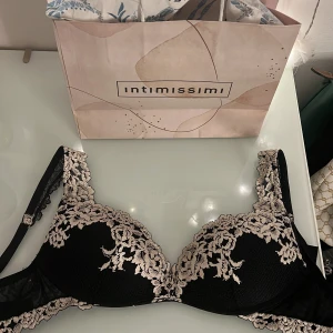 Svart spets bh från Intimissimi - Supersnygg svart bh från Intimissimi med beige spetsdetaljer och blommigt mönster. Axelbanden är dekorerade med spets och bh-n har en klassisk form med hakknäppning bak. Perfekt för dig som gillar eleganta och feminina detaljer. Har använts fåtal gånger💞Säljer denna pga att den passar inte riktigt, nypris: 519kr💗