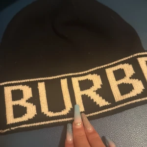 Svart Burberry mössa  - Säljer denna Svart stickade mössa från Burberry med vit logotyp (ser gult ut på bilden för ljusen men det är vit text)  runt hela kanten. Skriv för fler bilder osv💞💞