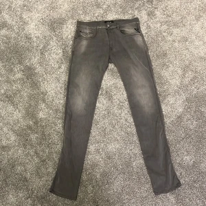 Replay grå slim jeans - Snygga grå jeans från Replay med slim passform och klassisk femficksdesign. Jeansen har diskreta slitningar och Replay-logga på bakfickan. Materialet är mjukt och stretchigt för extra komfort. Perfekt för dig som gillar stilrena och moderna jeans.