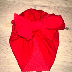 Röd turban med stor rosett Röd mössa - Söt röd turbanmössa med en stor rosett. Perfekt för att hålla barnets huvud varmt och samtidigt vara en snygg accessoar. Snygg röd turban med en riktigt stor rosett framtill. Mjuk och stretchig, perfekt för att ge din look lite extra edge. Materialet känns som polyester och färgen är intensivt röd. Passar dig som vill sticka ut och gillar statement-accessoarer. 🎄 