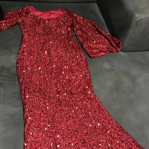 Röd glittrig långklänning med paljetter - Balklänning, Säljer en röd långklänning med glittriga paljetter över hela klänningen. Klänningen har lång ärm och en elegant, figurnära siluett som breddas nedtill. Perfekt för dig som vill sticka ut med en glamorös look.
