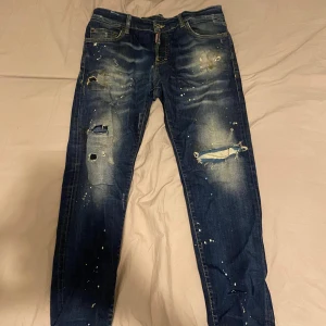 Dsquared2 blå distressed jeans - Snygga blå jeans från Dsquared2 med coola slitningar, hål och färgstänk med tydliga detaljer och logotyp på bakfickan. Jeansen har en smal passform och är tillverkade i jeansmaterial.