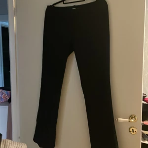 Svarta kostymbyxor från Bikbok - Snygga svarta kostymbyxor från Bikbok i storlek 38. Byxorna har utsvängda ben diskreta bakfickor och bälteshällor. Materialet är slätt och känns dressat, perfekt för en clean look. Passformen är normal och midjan är klassisk.