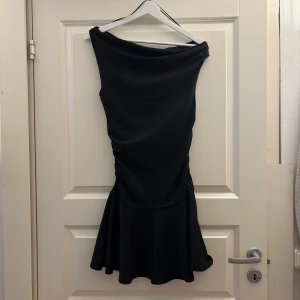 Svart asymmetrisk kort klänning M - Svart kort klänning med asymmetrisk halsringning och figurnära passform. Perfekt för dig som gillar stilrena och trendiga plagg med en twist. Aldrig använd med prislapp! 