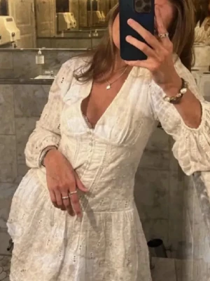 Vit kort klänning med spetsdetaljer - Superfin vit kortklänning med v-ringning och broderade spetsdetaljer. Klänningen har långarm men går ihop vid vristerna. Perfekt för sommaren, student och utomlandsresa.